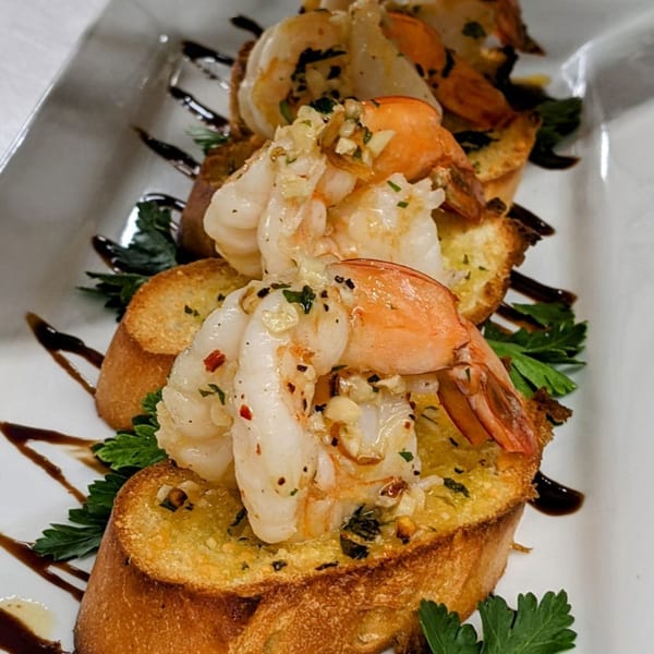 Garlic shrimp bruschetta with parsley and balsamic glaze on a white rectangular plate.