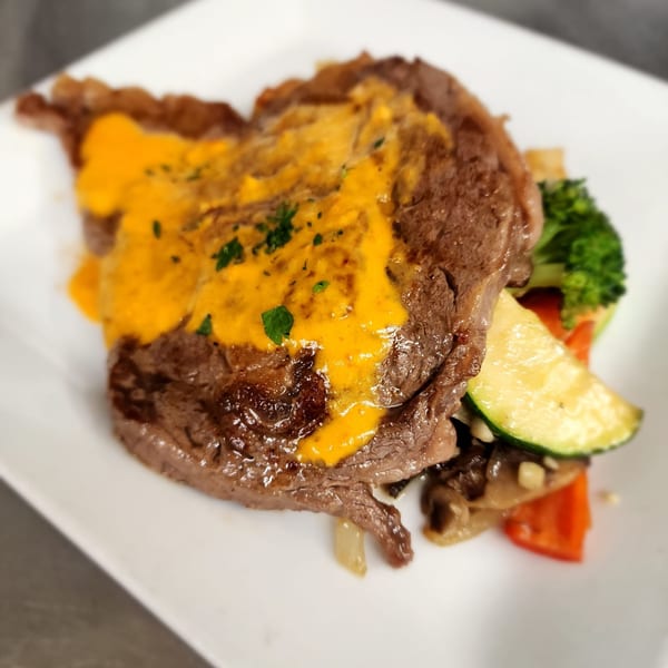 A steak with orange sauce and parsley, served with broccoli, zucchini, and mushrooms.