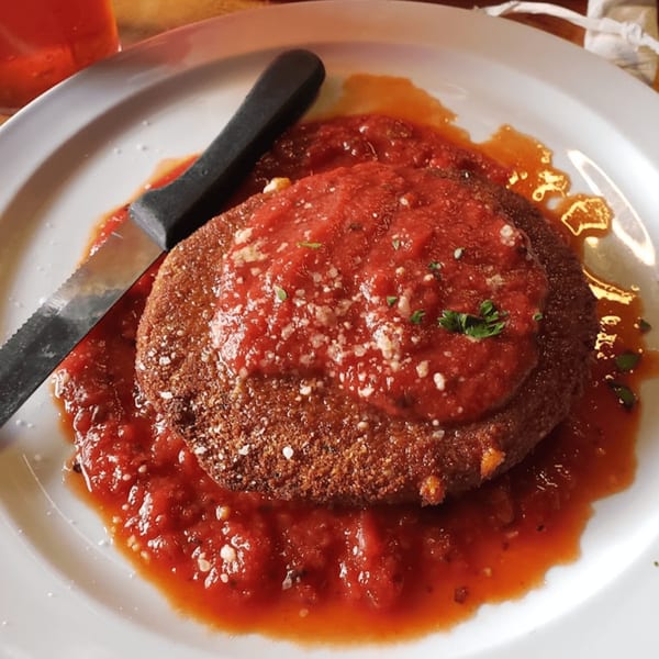 Pizzeli's Italian Oven's fried eggplant parmesan, topped with red sauce, cheese, and parsley, with a knife.