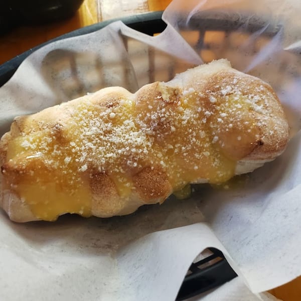 A golden-brown breadstick, generously topped with melted cheese and grated Parmesan, rests in a basket.