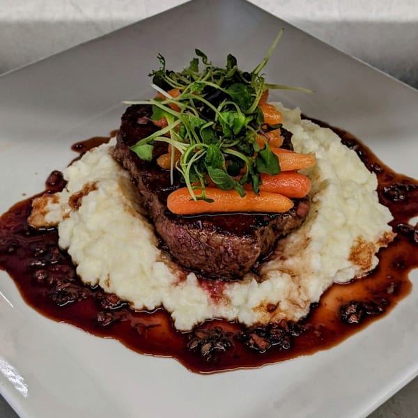 Pizzeli's Italian Oven steak with mashed potatoes, baby carrots, microgreens, and a rich sauce.