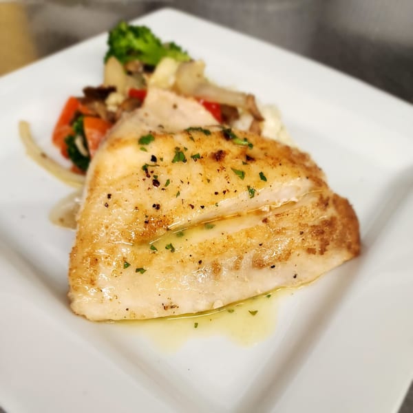 Pan-seared fish fillet with herbs, served with roasted vegetables on a white plate.